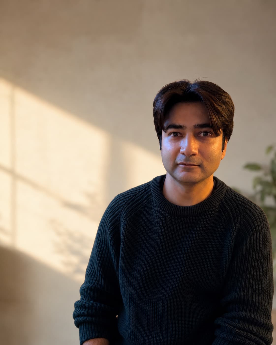 Portrait of Jahanzaib Suleman in a dark sweater, lit by warm golden-hour window light.